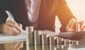 Image of accountant making calculations via pen and paper, as well as calculator. 